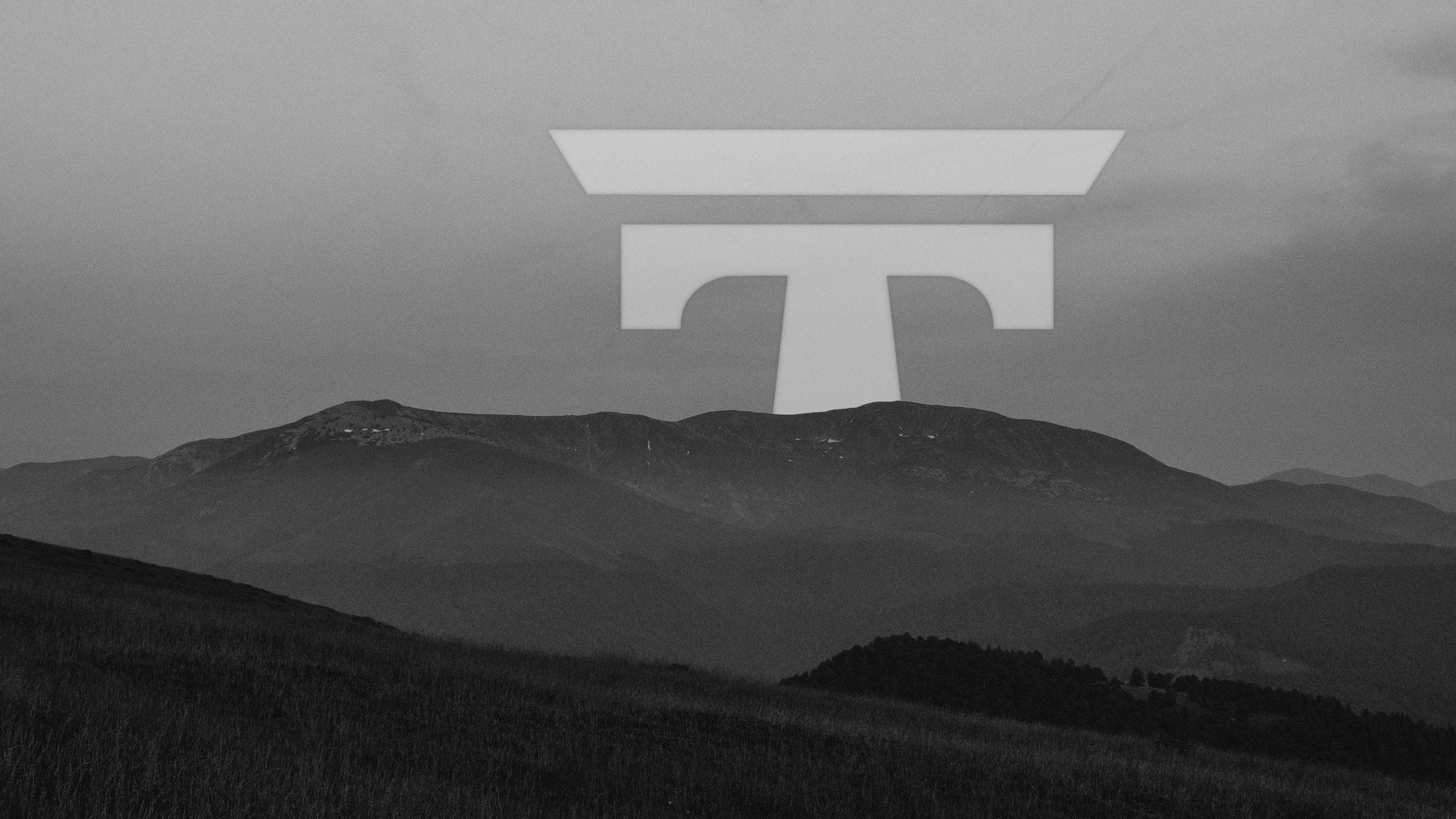 Black and white landscape with geometric T logo floating above mountains